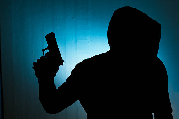 Silhouetted man with gun against blue wall background